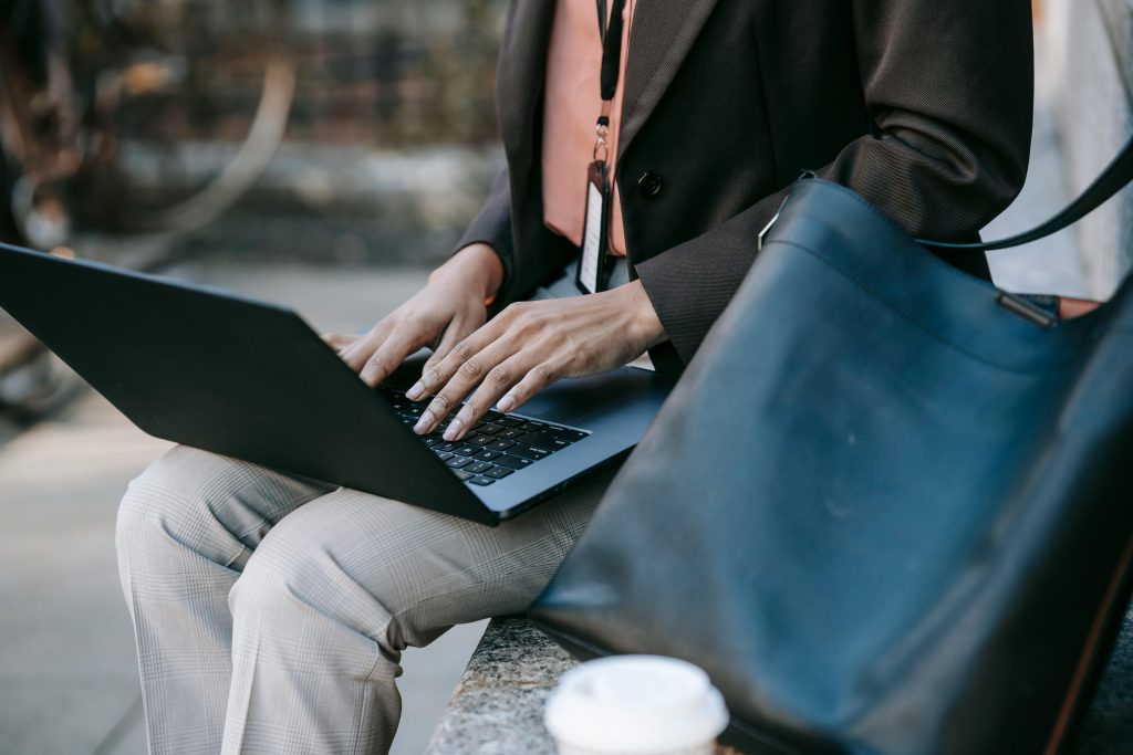 Crop unrecognizable female freelancer with badge typing on laptop keyboard while working on new project